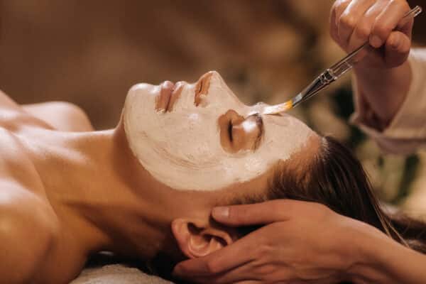 A cosmetologist makes a mask for a womans face to rejuvenate the skin
