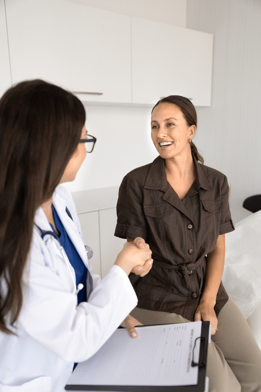 Doctor in a white coat shakes hands with a smiling patient in a bright clinic, clipboard in hand
